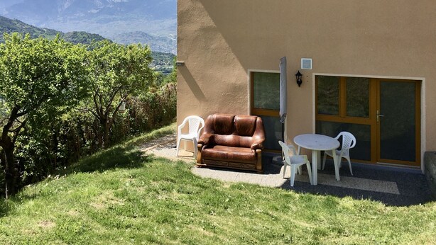 A modern building with a brown exterior, a brown leather couch, and a small round table with two white plastic chairs. - Petit Appartement à Louer Dans le Val Dhérens (Vernamiège)