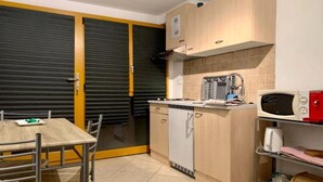 A compact kitchen with a dining area, including a microwave, toaster, and a small refrigerator. - Petit Appartement à Louer Dans le Val Dhérens (Vernamiège)