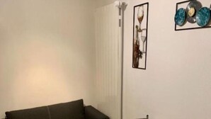 A room with a dark-colored sofa, a wooden dining table with metal chairs, and two wall-mounted artworks. - Petit Appartement à Louer Dans le Val Dhérens (Vernamiège)