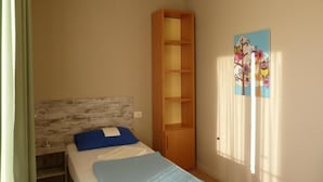 A bedroom with a bed, a wooden wardrobe, a window with curtains, and a wall with a floral painting. - Ostello Torino (Turin)