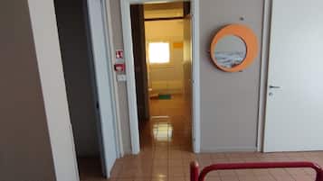 Ein Hotelzimmer mit Bett, Badezimmertür, einem zur anderen Kammer führenden Gang und einem runden Spiegel an der Wand.