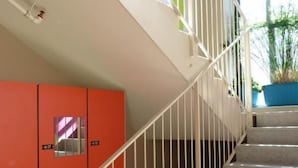 A staircase with white railings leading to a landing with colorful walls and a potted plant. - Ostello Torino (Turin)