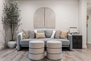 Uma sala de estar moderna com um sofá cinzento, almofadas estampadas e um objeto decorativo na parede.