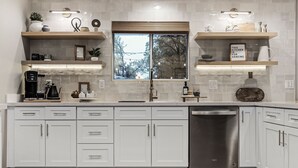 Una cocina moderna con armarios blancos, un lavavajillas de acero inoxidable y un ventanal grande.