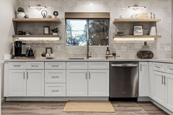 A modern kitchen with white cabinets, a stainless steel dishwasher, and a large window.
