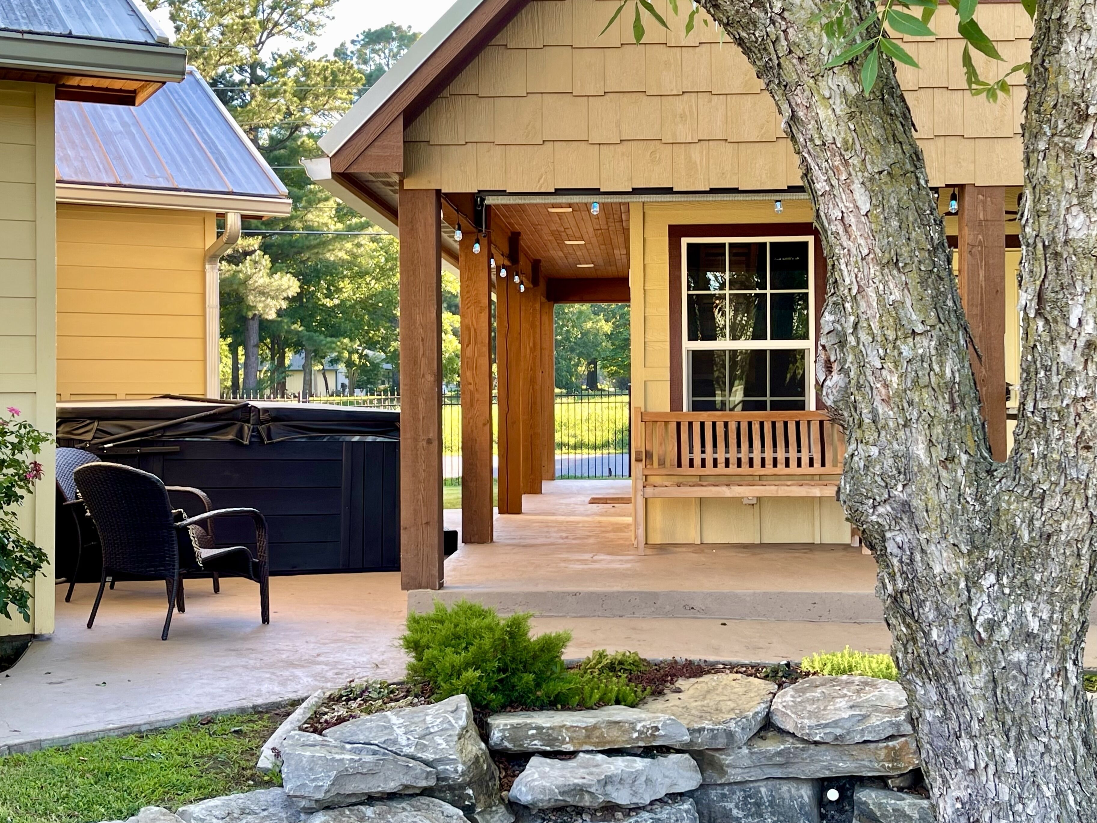 A covered patio area with outdoor furniture, a stone wall, and a view of a residential property.