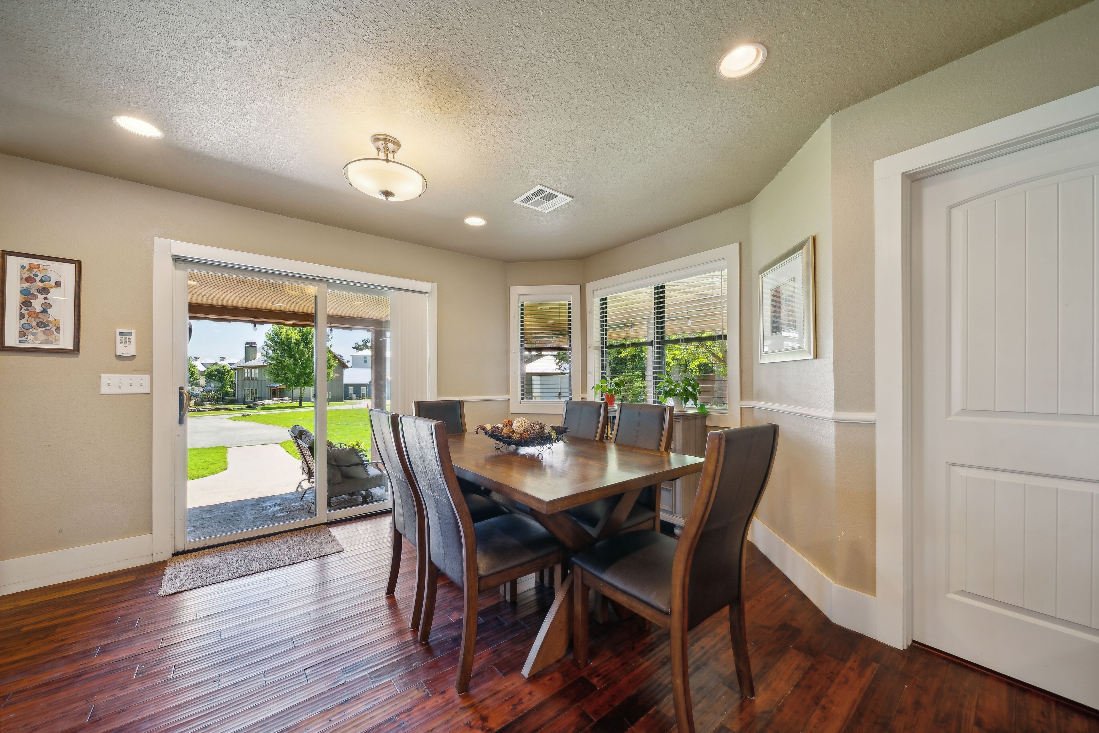 A dining area with a wooden table and chairs, a sliding glass door leading outside, and recessed ceiling lights.