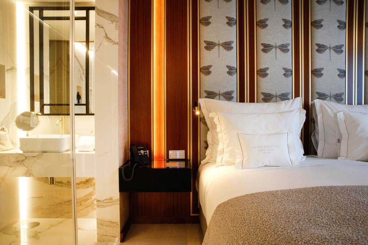 A hotel room with a marble bathroom, a bedside telephone, and a bed with white bedding.