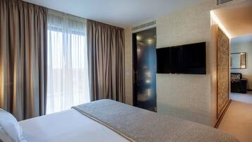 A hotel room with a large bed, a flat-screen TV mounted on the wall, and a large window with curtains.