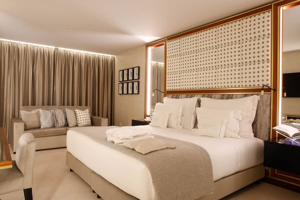 A modern hotel room with a large bed, a sofa, and a desk with a lamp.
