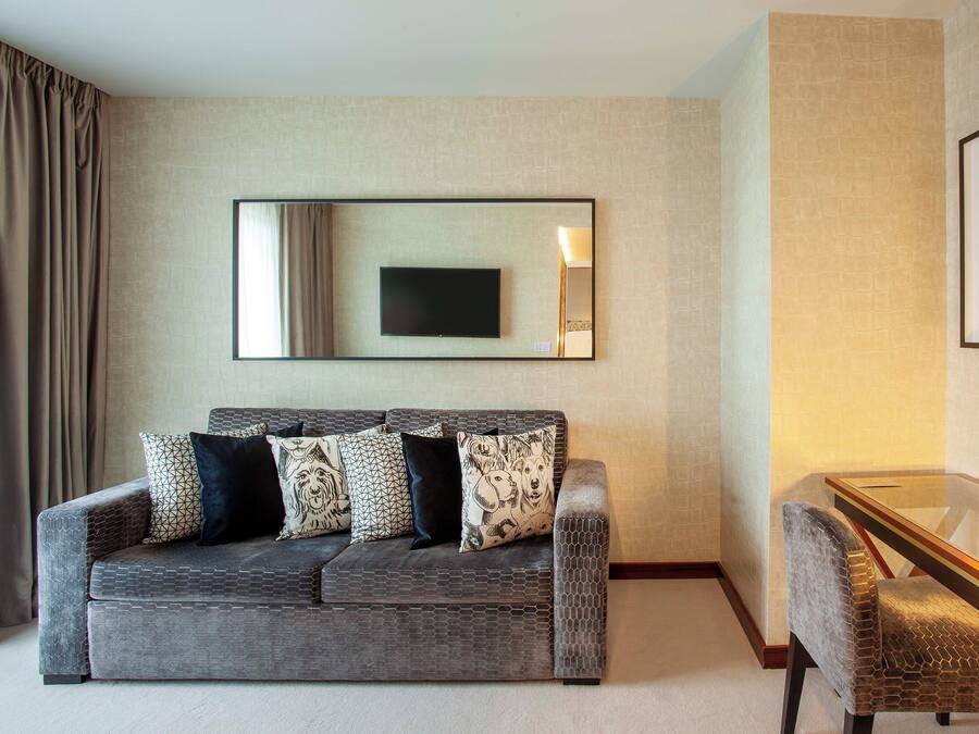 A modern living room with a grey sofa, patterned cushions, a flat-screen TV, and a glass coffee table with a sculpture.
