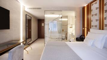 Une chambre d’hôtel moderne dotée d’un grand lit, d’une douche en verre, d’un bureau avec une chaise et d’un grand miroir.