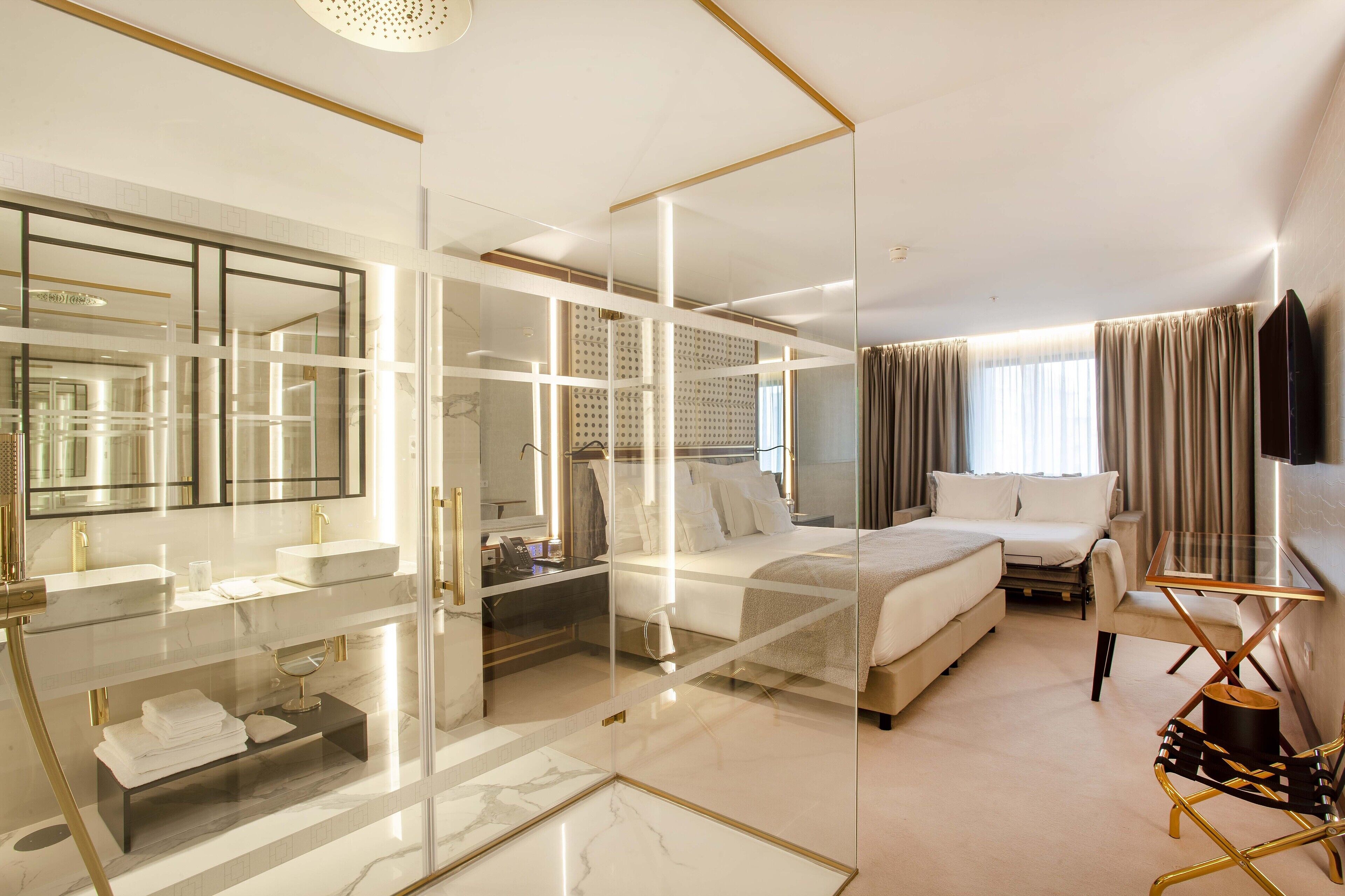 Una habitación de hotel moderna con armario de vidrio, cama grande, zona de estar y televisor de pantalla plana.