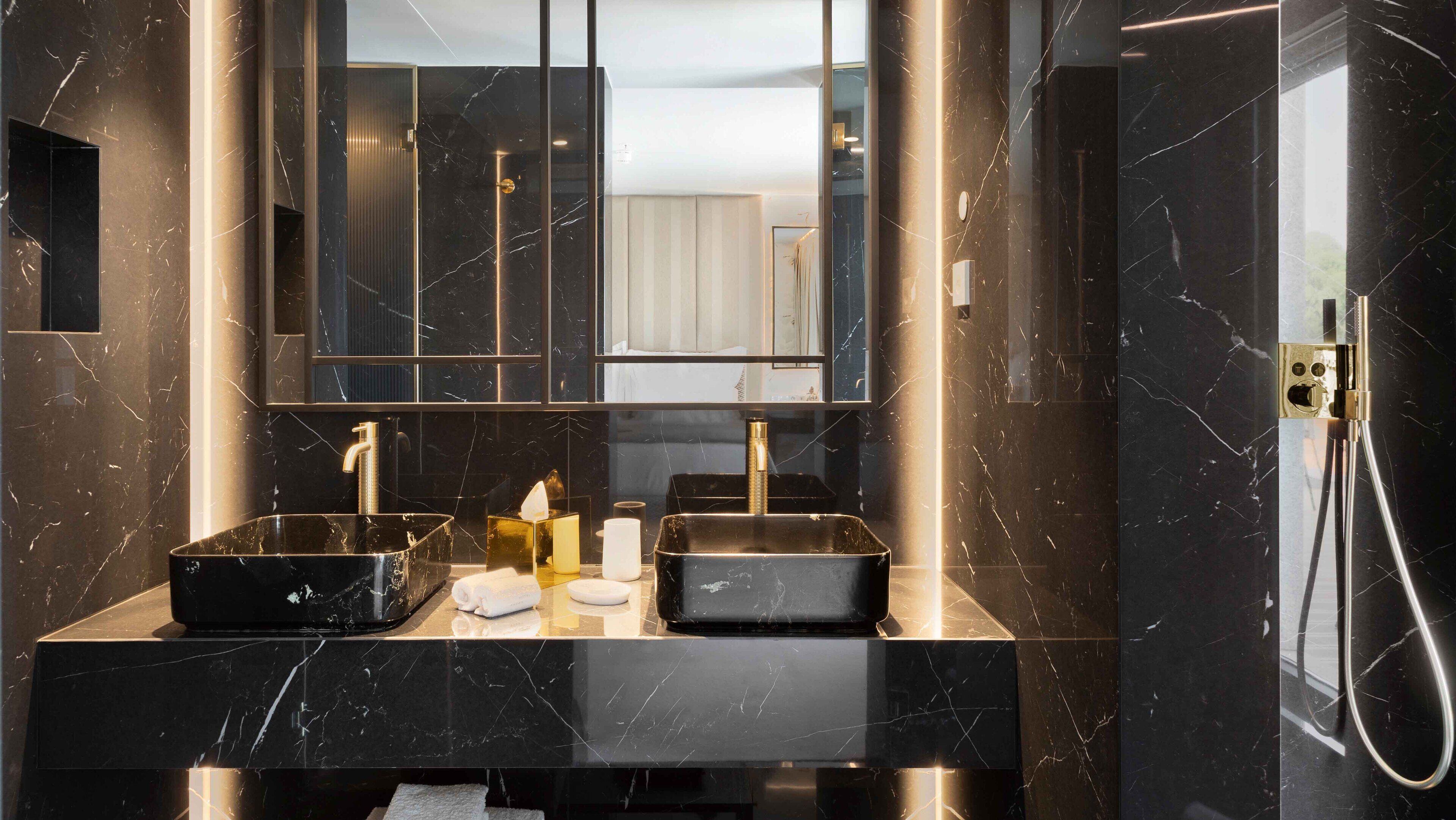 Un baño moderno con dos lavamanos de mármol negro, un espejo grande y un cabezal de ducha manual.