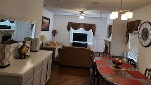 A living room with a fireplace, a dining area with a table set for four, and a kitchen area with cabinets and a refrigerator. - House of Comfort, A centrally located 4 bedroom home. (Duncanville)