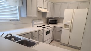 A kitchen with white cabinets, a stove, a microwave, and a refrigerator. - House of Comfort, A centrally located 4 bedroom home. (Duncanville)