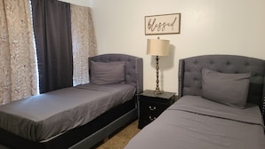 A room with two single beds, a nightstand with a lamp, and a 'blessed' sign on the wall. - House of Comfort, A centrally located 4 bedroom home. (Duncanville)