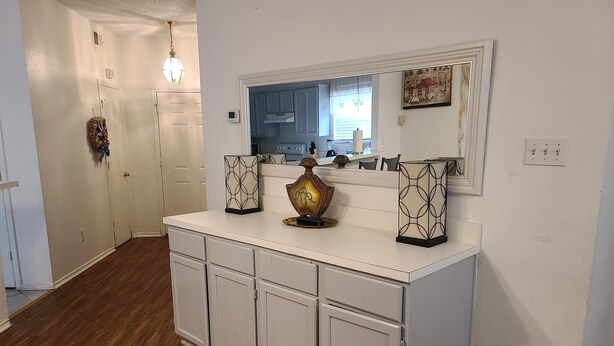 A kitchen with white cabinets, a wooden floor, and a large mirror above the counter. - House of Comfort, A centrally located 4 bedroom home. (Duncanville)