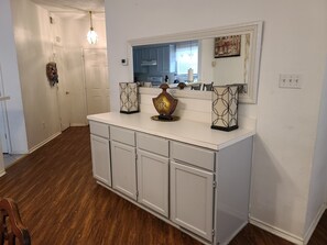 Una cocina con armarios blancos, suelo de madera y un espejo grande sobre el mostrador.