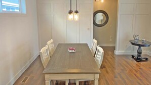 Une salle à manger avec une table en bois, des chaises blanches, des luminaires suspendus, un miroir rond et une petite table sur laquelle se trouve une carafe.