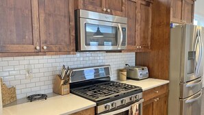 Une cuisine dotée de meubles en bois, d’un four à micro-ondes en acier inoxydable, d’un grille-pain, d’une cuisinière et d’un réfrigérateur.