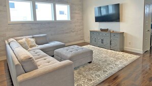 Un salon moderne avec un canapé d’angle, un téléviseur à écran plat et un meuble gris.