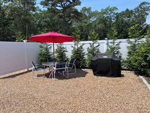 Une terrasse avec une table et des chaises, un parasol rouge et un barbecue.