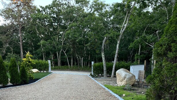 Un camino de grava que conduce a una casa rodeada de árboles y un jardín.