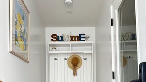 Un pasillo con un banco blanco, un sombrero colgado en la pared y un cartel que dice "SUMMER".