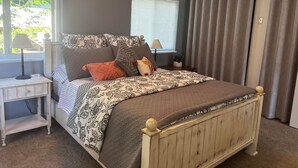 Ein Schlafzimmer mit einem Bett, Nachttischen, einem Fenster mit Jalousien und einem Vorhang.