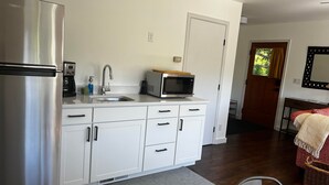 Eine kleine Küche mit weißen Schränken, einem Edelstahlkühlschrank, einer Mikrowelle und einer Kaffeemaschine.
