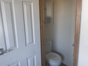Et lille, smalt badeværelse med en hvid dør, et hvidt toilet og en træramme.