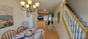 Un coin repas avec une table dressée pour quatre personnes, un lustre et un escalier menant à l’étage supérieur.