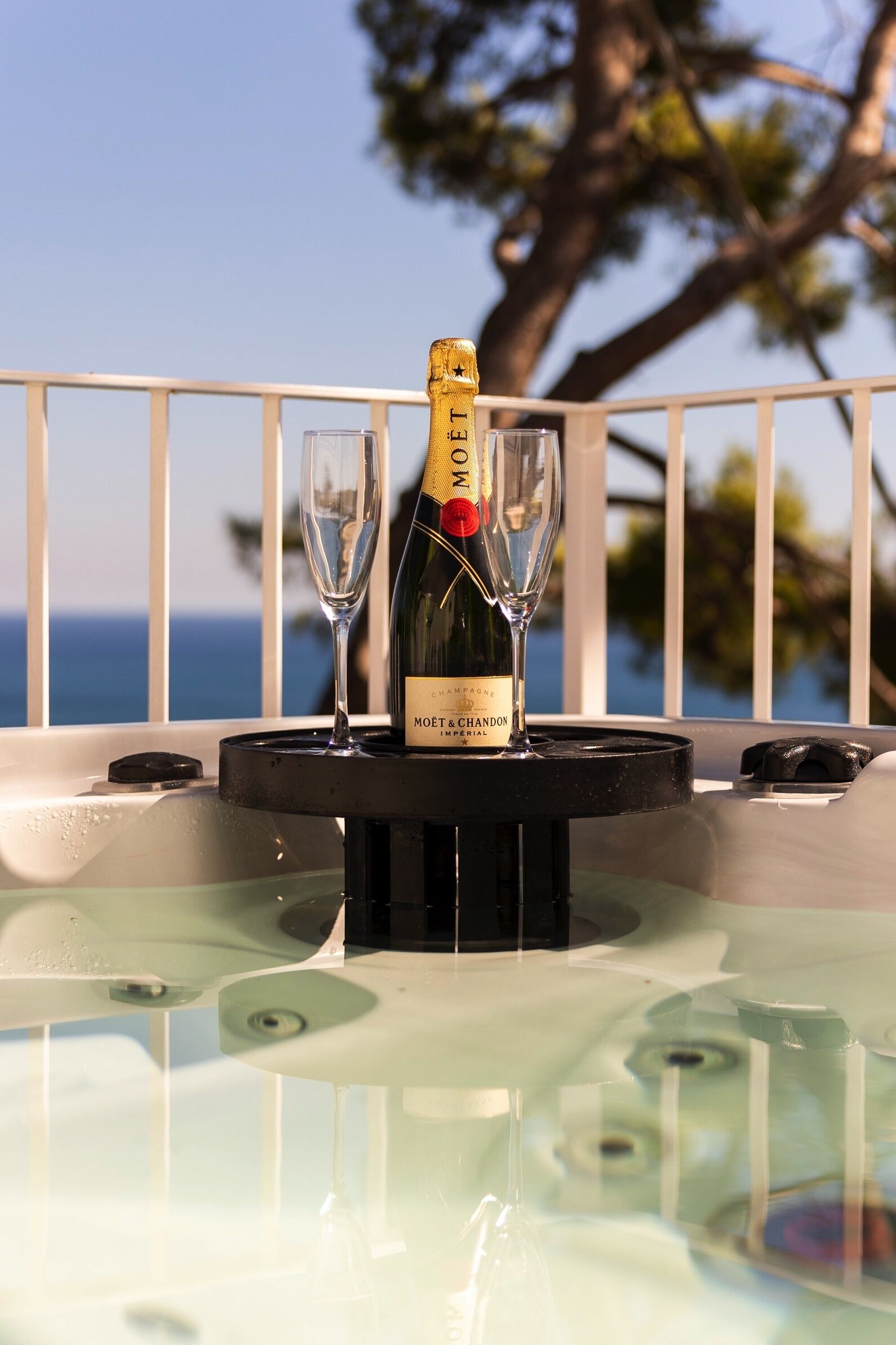 A bottle of Moët & Chandon champagne on a table with two glasses, set against a balcony with a view of the sea.