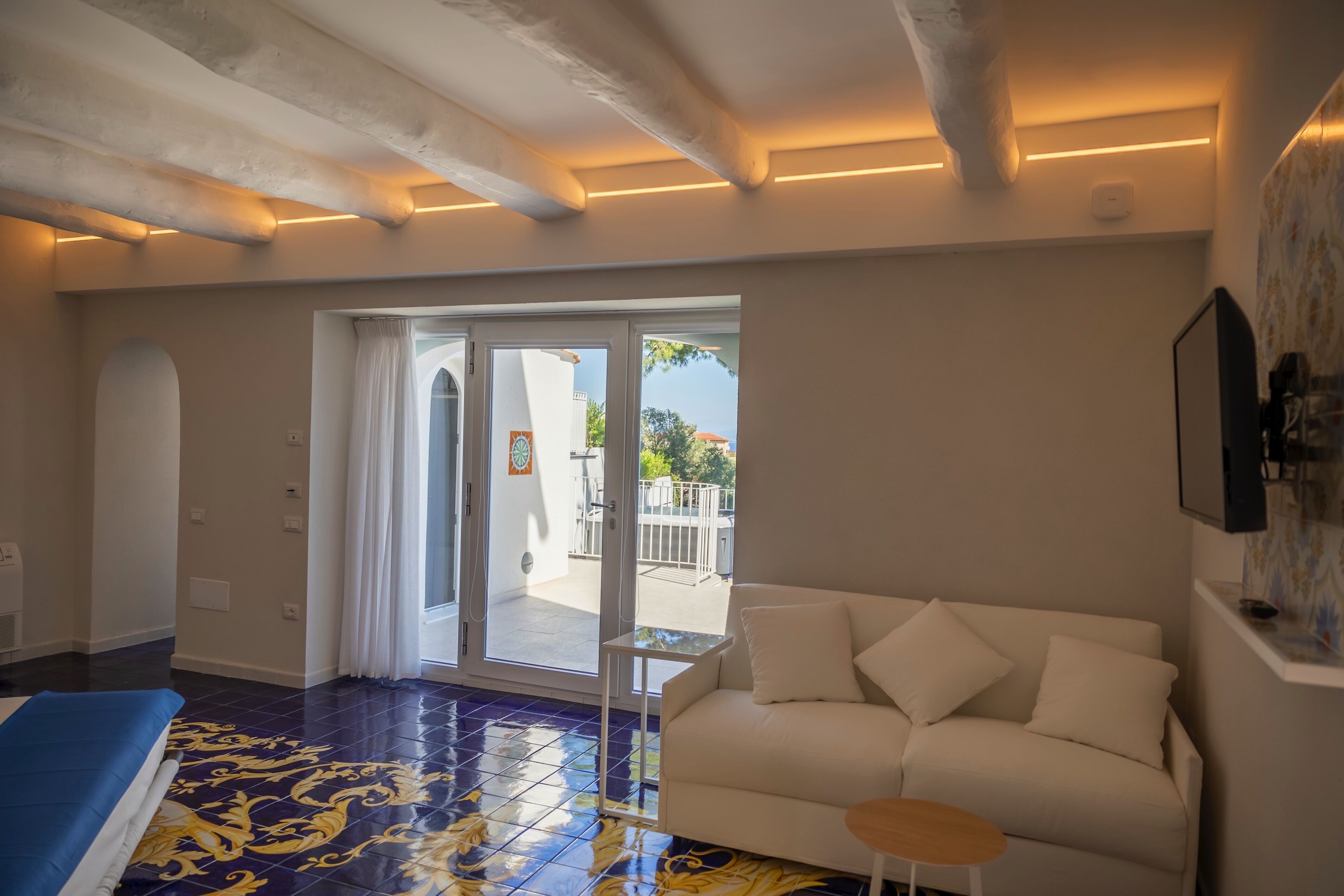 A hotel room with a large bed, a white sofa, a small table, and a balcony with a view.