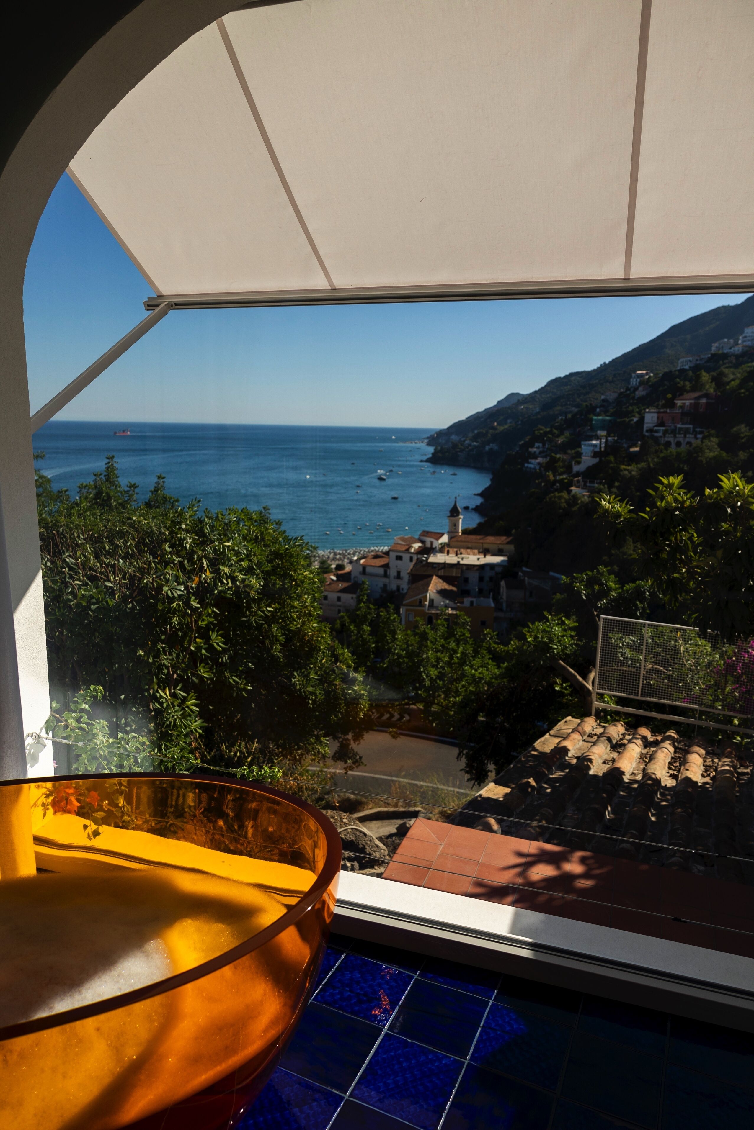 A balcony with a view of the sea, buildings, and greenery.