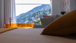 Un dormitorio con cama, ventana y vista a la montaña, y un almohadón amarillo.