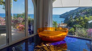 Una habitación con un amplio ventanal que da a un balcón con vistas al mar y las colinas.