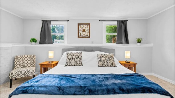 Um quarto com uma cama grande, duas mesas de cabeceira, uma cadeira e uma janela com cortinas.