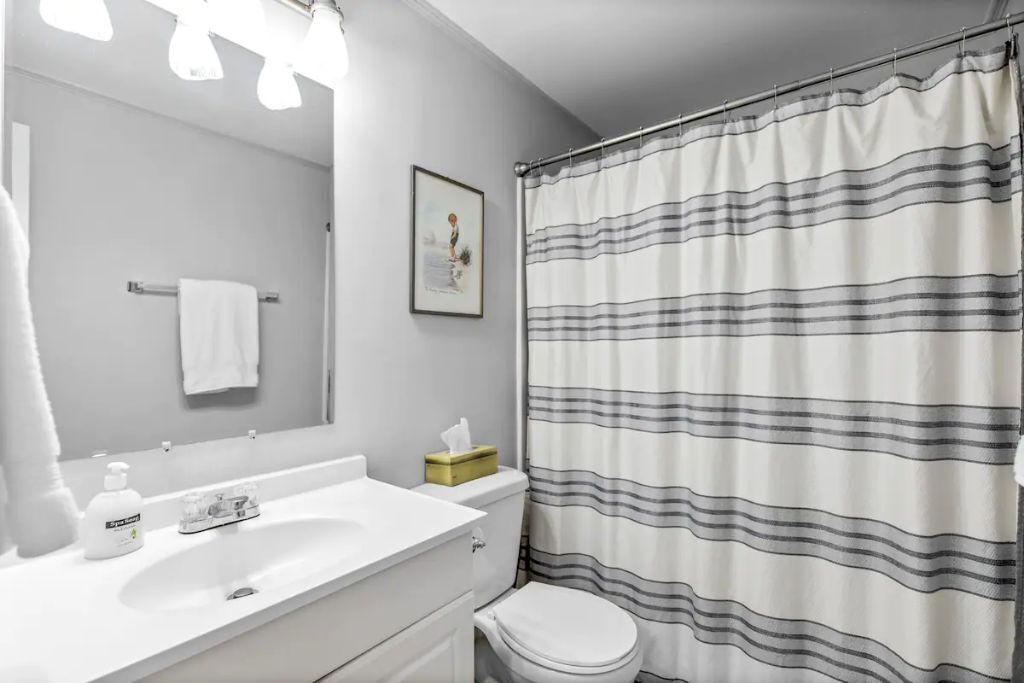 Een badkamer met een witte wastafel, een spiegel, een toilet en een douchegordijn met strepen.