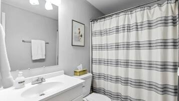 Een badkamer met een witte wastafel, een spiegel, een toilet en een douchegordijn met strepen.