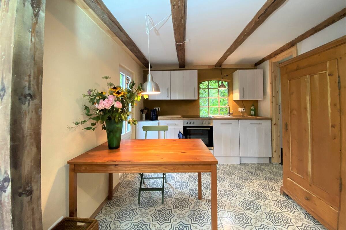 Una cocina con armarios blancos, una mesa de madera y un suelo con diseño.