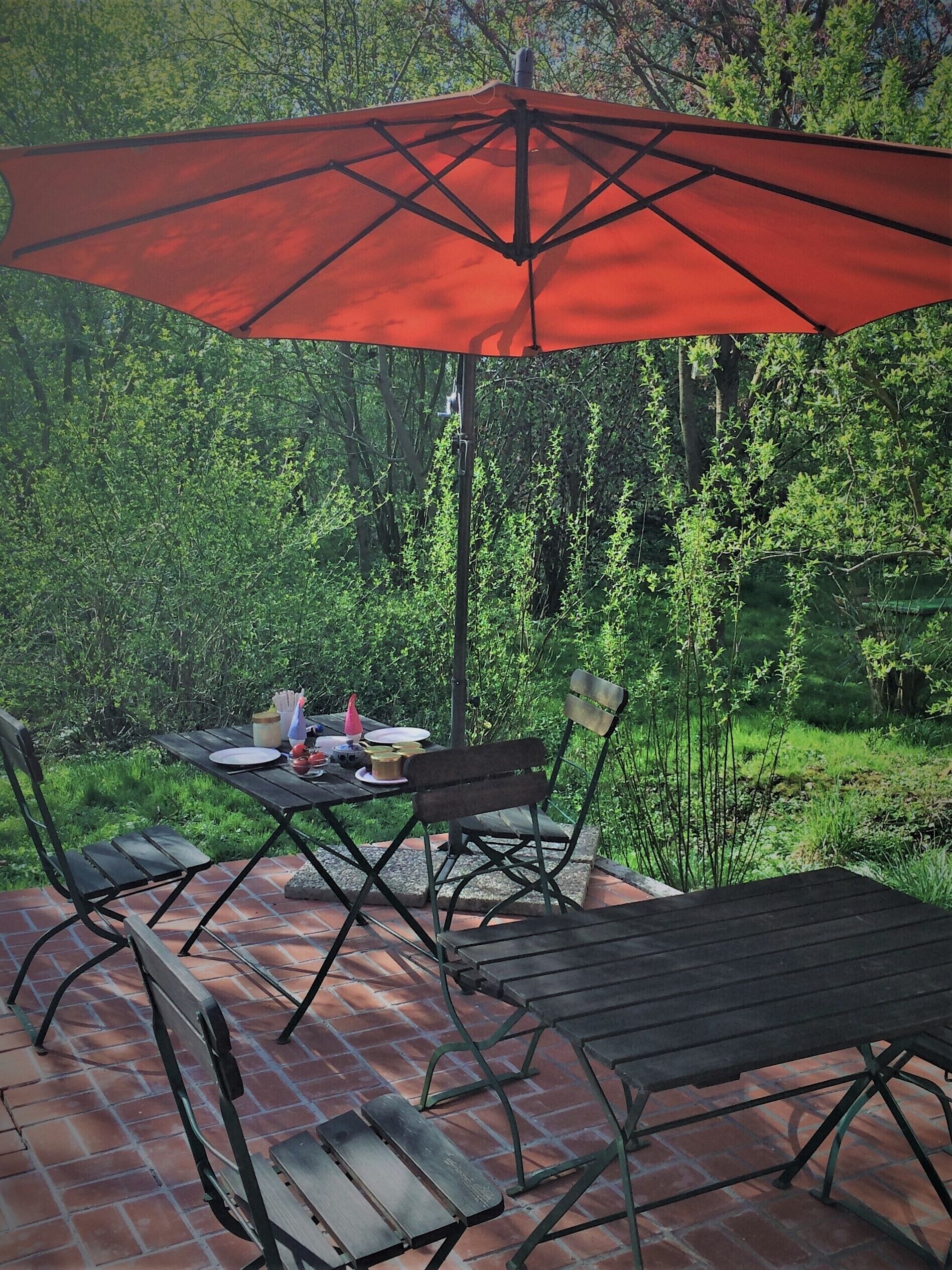 An outdoor patio with a table and chairs, a red umbrella, and a brick floor.