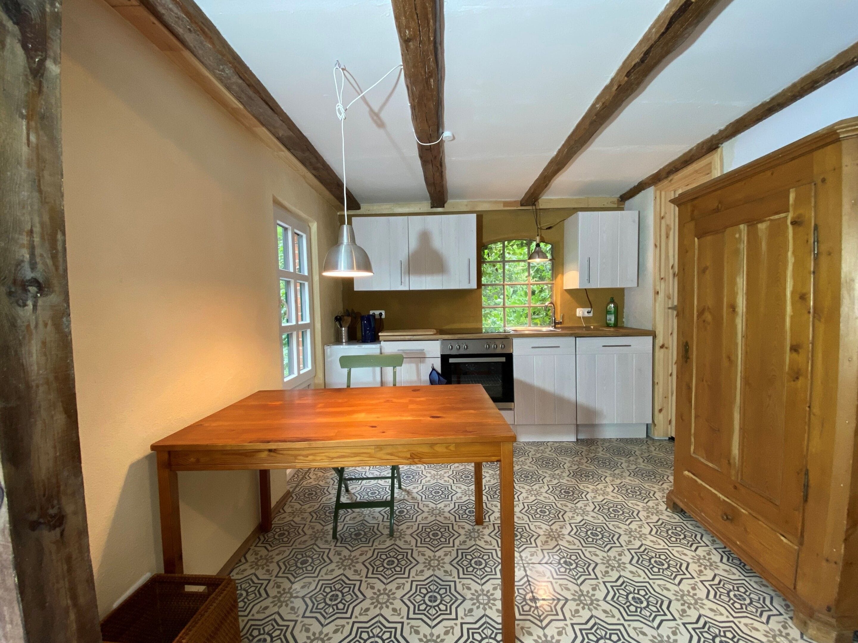 A kitchen with a wooden table, cabinets, and patterned floor tiles.