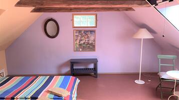 Una camera da letto con soffitto spiovente, un letto con copriletto a righe, una piccola panca, una sedia, una lampada da terra e un quadro appeso al muro.