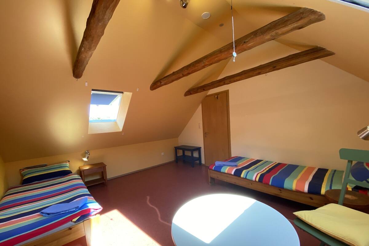Una habitación pequeña y acogedora con dos camas, una mesa redonda y un ventanal.