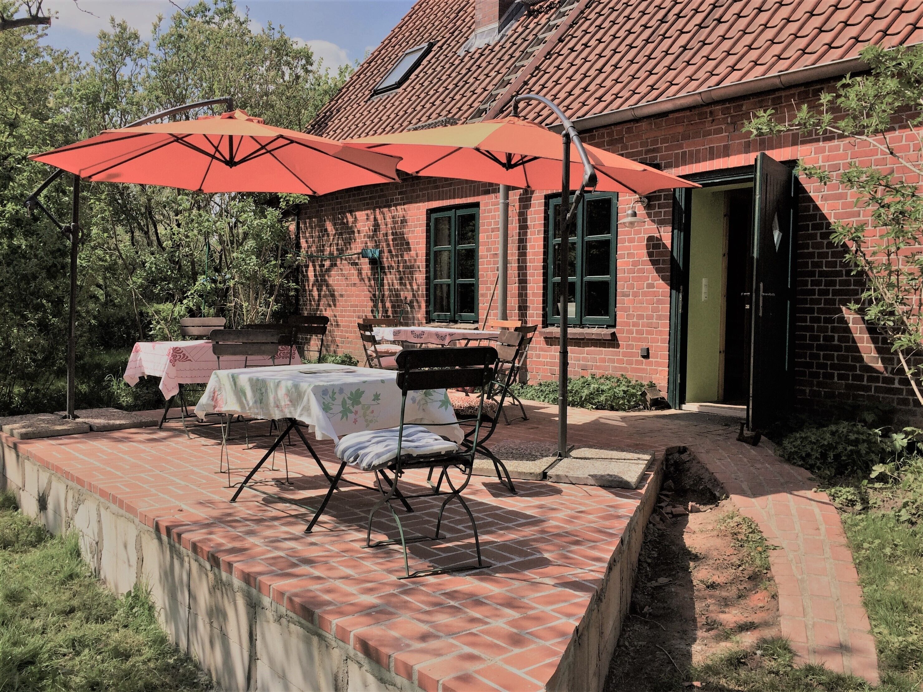 A patio with a brick table and chairs, two red umbrellas, and a brick building in the background.