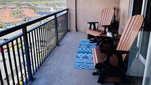 Un balcon donnant sur un quartier résidentiel, un tapis bleu à motifs et deux chaises en bois.