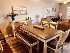 A dining area with a wooden table, benches, and chairs. There is a vase with plants on the table, and a painting on the wall. - 3 BEDROOM LAKE & GOLF VIEW CONDO| SHORT WALK TO THE BEACH| UNIT 1114 (North Myrtle Beach)