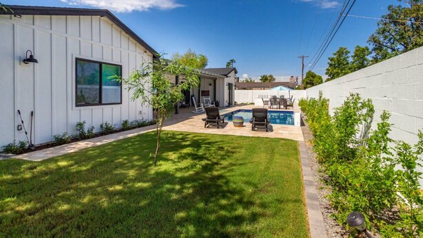 Un cortile residenziale con piscina, un piccolo albero e un edificio bianco.